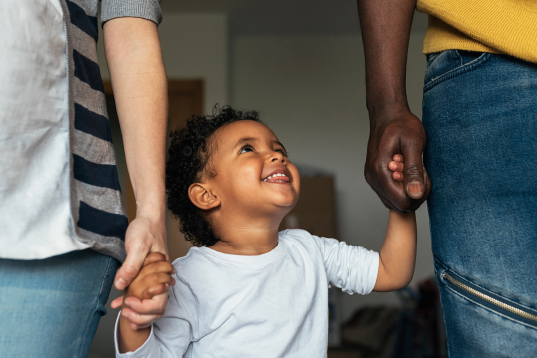 Child smiles holding his parents hands. 