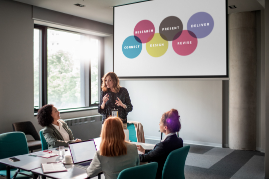 A businesswomen presents to group of employees sat around a table.