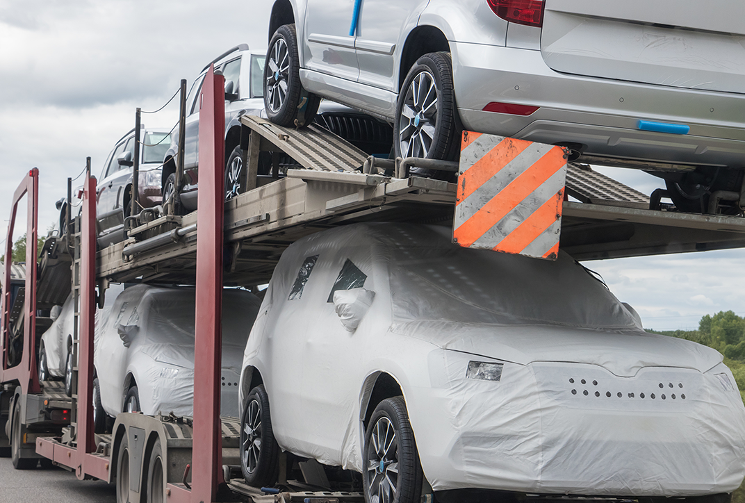 Cars covered in protective film being transported on a railroad wagon.