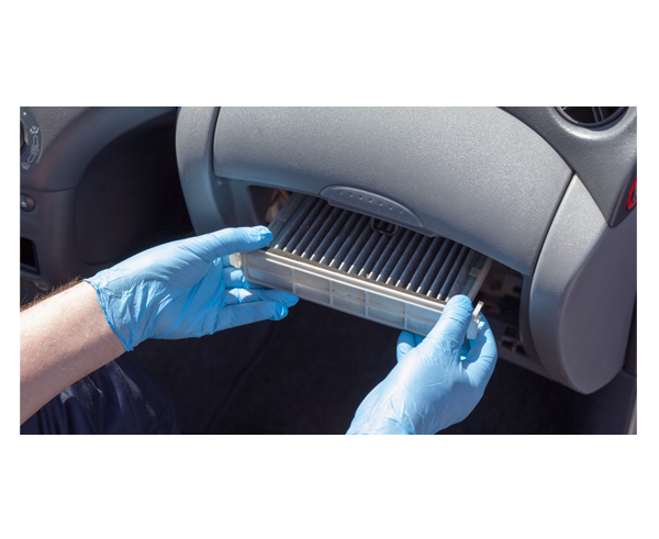 A person wearing protective gloves replacing the filter in a car ventilation system.