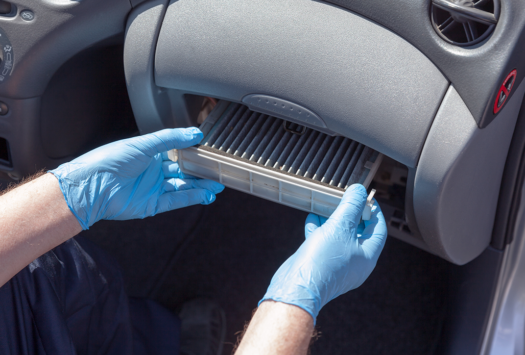 A person wearing protective gloves replacing the filter in a car ventilation system. A person wearing protective gloves replacing the filter in a car ventilation system.