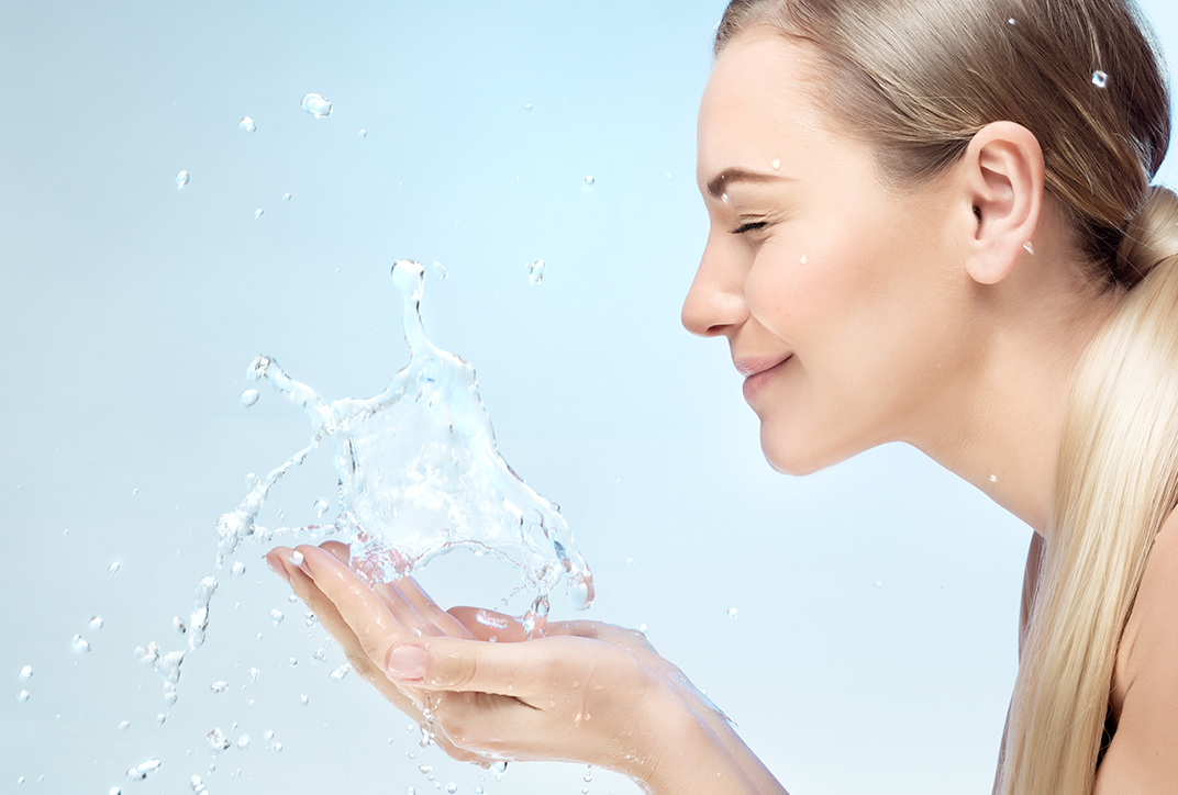 A lady splashing water onto her face with both hands.