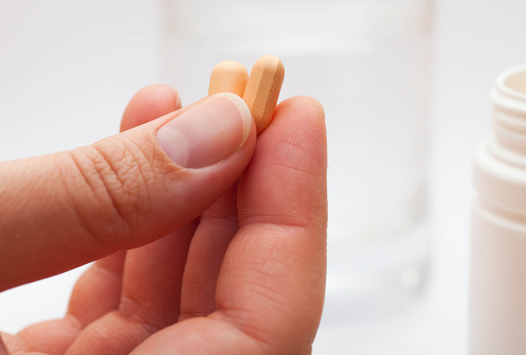 A hand holding two orange tablets.