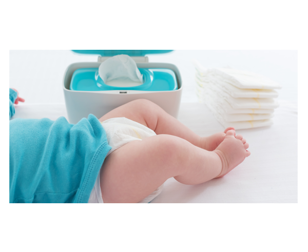 Der Unterkörper eines Babys auf einem Wickeltisch. Im Hintergrund steht ein Spender mit Feuchttüchern, daneben ist ein Stapel Windeln.