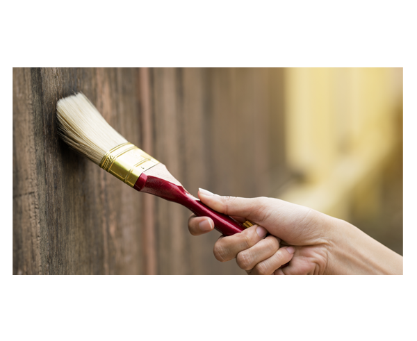The photo shows a hand painting a fence with a paintbrush.