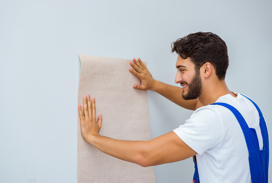 A man holding a piece of wallpaper against a wall.